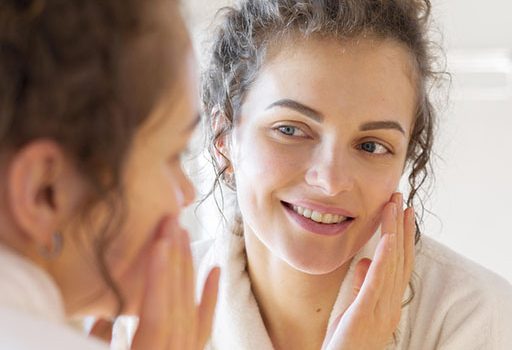 Mulher olhando seu rosto após tratametno de Acne